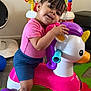 Antonielys is registered to the contest to win money with this photo: toddler, child, unicorn_toy, ride_on_toy, pink_shirt, blue_shorts, socks, colorful_toy, foam_mat, indoor, playtime, smiling, happy, cute, home, living_room, plastic_toy, purple_wheels, yellow_horn, playful