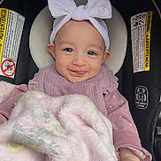 Layla is registered to the contest to win money with this photo: baby, child, smiling, headband, bow, blanket, car_seat, clothing, pink, face, infant, cute, happy, indoors, person, portrait, seat, warning_label, soft, toddler