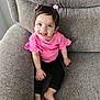 barefoot, black_pants, bright, casual, child, couch, cozy, cute, furniture, hair_bows, happy, home, indoor, person, pink_top, portrait, sitting, smiling, toddler, young_child