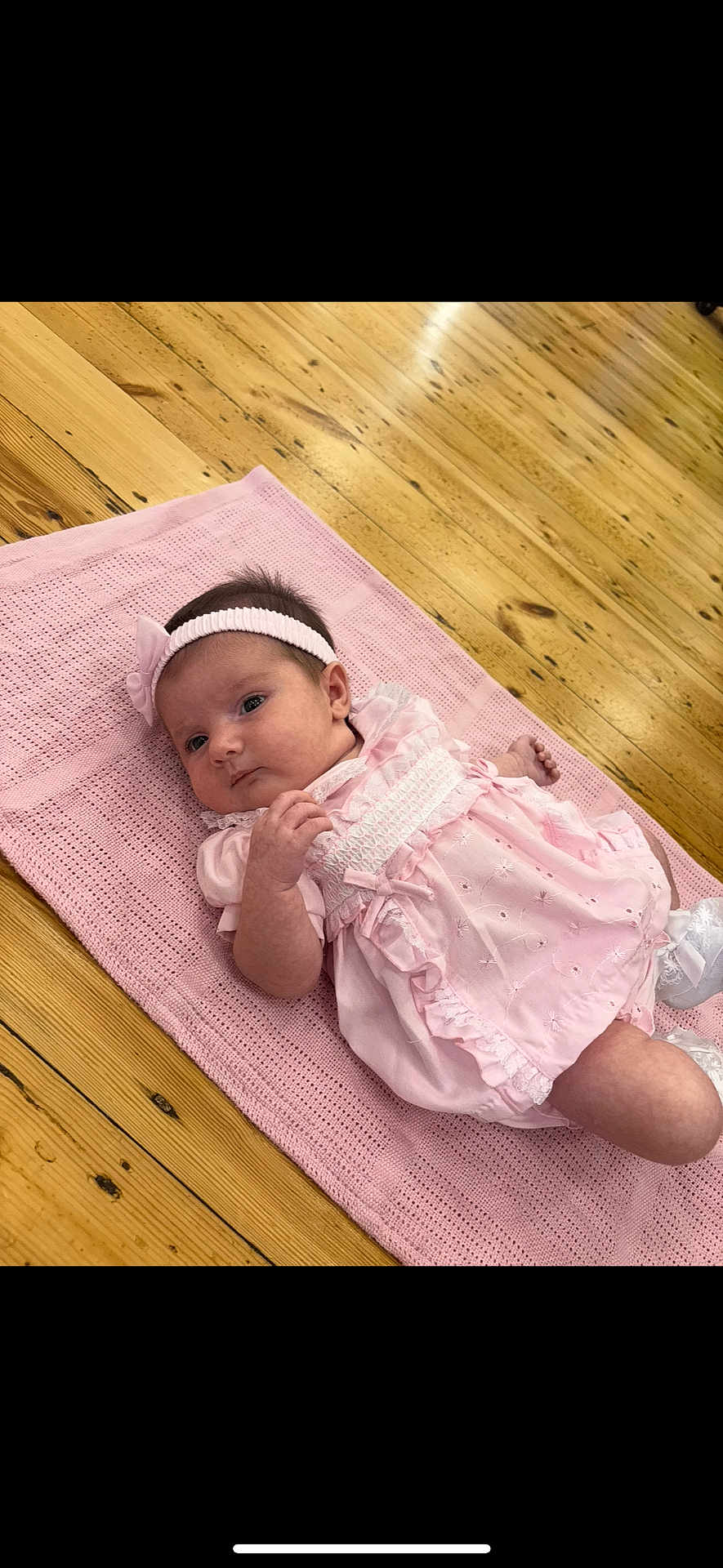 Hallie is registered to the contest to win money with this photo: baby, infant, pink_dress, headband, blanket, wooden_floor, cute, lying_down, indoors, child, newborn, soft_lighting, portrait, smiling, young_child, cozy, comfortable, fashion, adorable, person