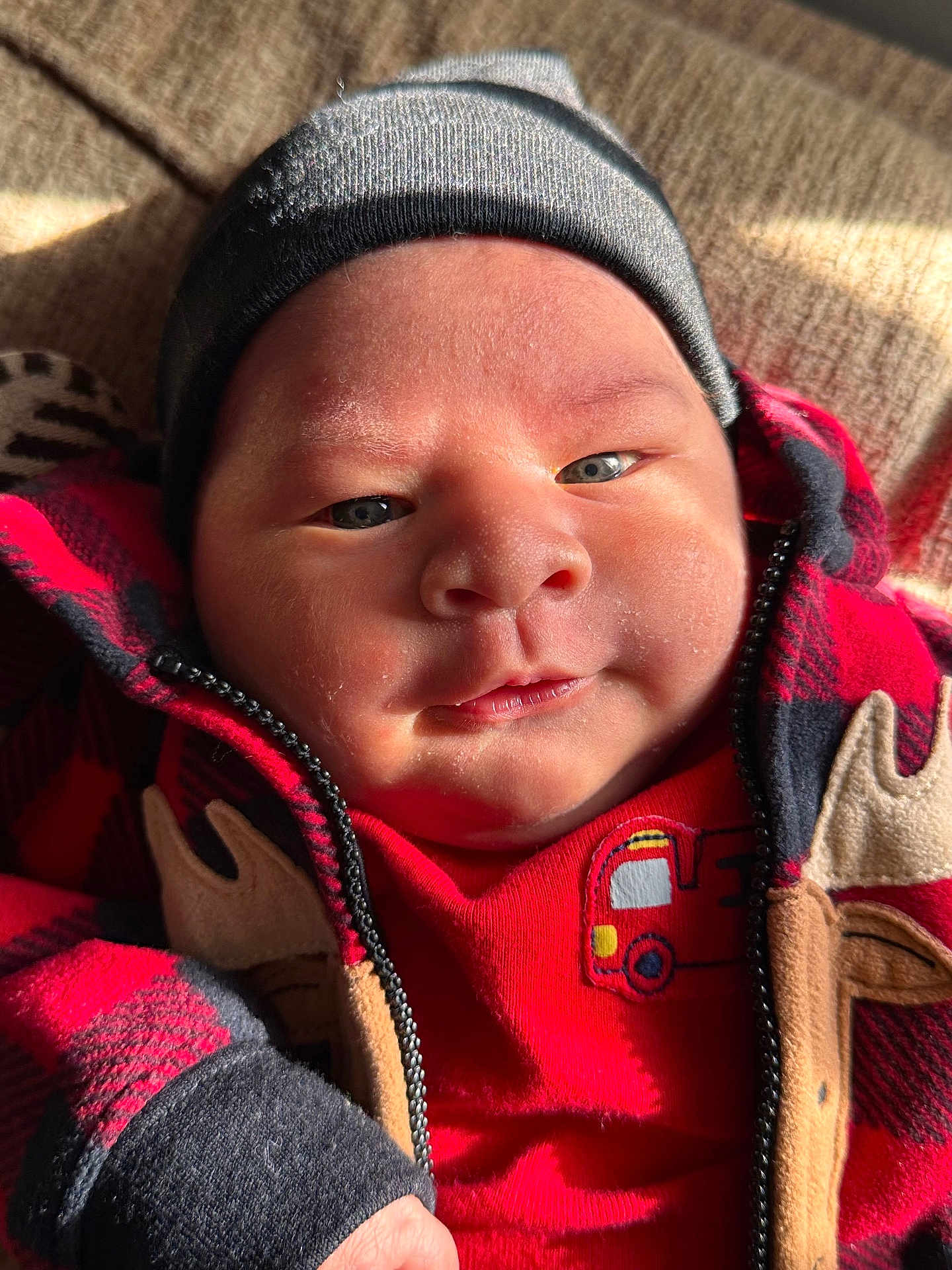 Joao joined the competition — help win amazing prizes! baby, infant, face, clothing, hat, beanie, jacket, red, black, plaid, closeup, skin, cheeks, eyes, sunlight, warm, cozy, cute, child, portrait