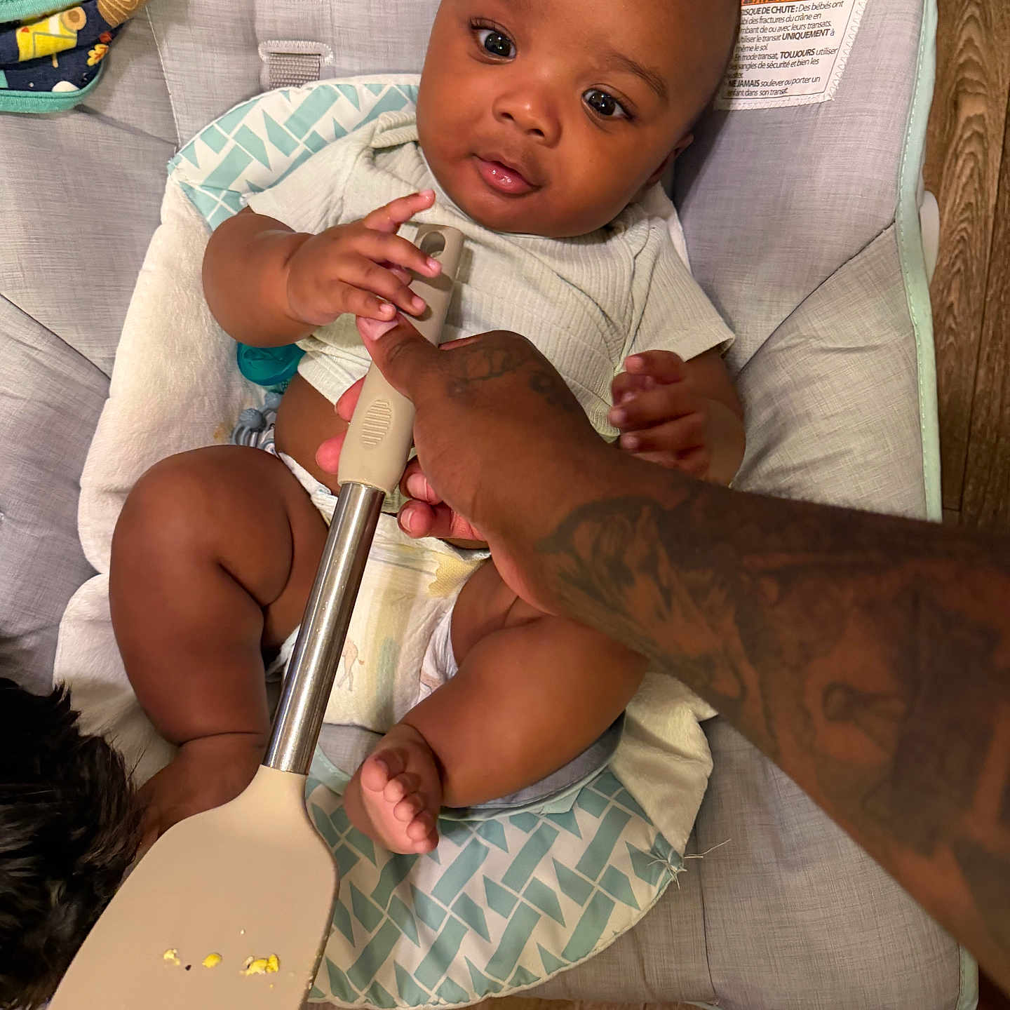 Genesis joined the competition — help win amazing prizes! baby, infant, child, cushion, seat, spatula, hand, tattoo, food, floor, blanket, wooden_floor, curious, indoors, clothing, diaper, skin, face, eyes, mouth