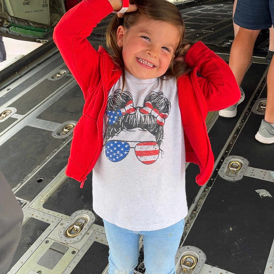 Braelin joined the competition — help win amazing prizes! aircraft_interior, american_flag, cargo_hold, casual_clothing, child, floor, hair, happy, jeans, lighting, metal, people, person, playful, pose, red_jacket, smiling, sneakers, standing, tshirt