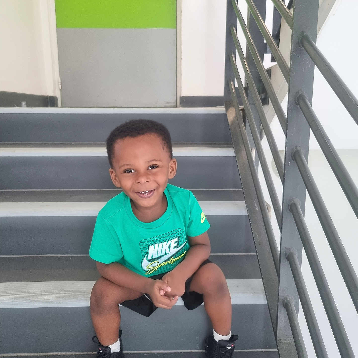 Robbins a rejoint le concours — aidez-le/la à gagner de superbes lots ! black_shoes, black_shorts, boy, casual_clothing, child, concrete_stairs, door, green_tshirt, happy, indoors, modern, nike, playful, portrait, railing, sitting, smiling, stairs, white_socks, young_child
