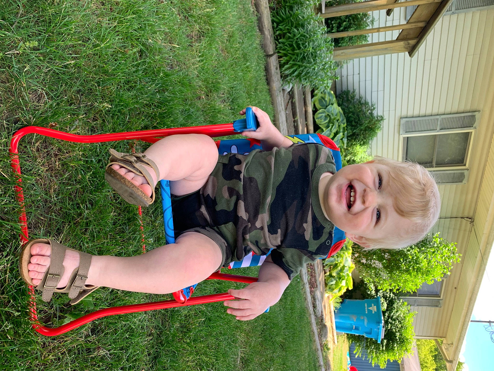 Malcolm is registered to the contest to win money with this photo: acrobatics, aerialist, balance, entertainment, fun, grass, green, happy, human_leg, knee, leg, leisure, outdoor_play_equipment, person, plant, recreation, shorts, smile, thigh, toddler