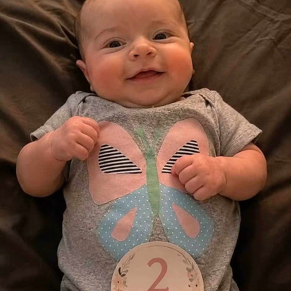 Alaysia is registered to the contest to win money with this photo: baby, infant, smiling, onesie, butterfly, milestone, 2_months, lying_down, cute, happy, child, skin, person, newborn, small, portrait, clothing, indoors, blanket, celebration