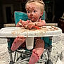 toddler, high_chair, chocolate, messy, face_paint, spoon, food, child, foot, table, indoor, curly_hair, blue_eyes, pink_clothing, baby, mess, kitchen, feeding_time, cute, expression