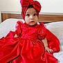 baby, child, red_dress, headband, bow, sitting, bed, indoors, portrait, cute, infant, clothing, fabric, face, eyes, hands, young_child, fancy, dress, curious