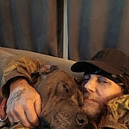 Diesel is registered to the contest to win money with this photo: animal, beard, bond, camouflage, cap, closeup, cozy, curtains, dog, face, hand, indoor, jacket, man, pet, portrait, relaxed, snuggling, tattoo, warm