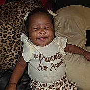 Teliyah is registered to the contest to win money with this photo: baby, smiling, girl, infant, cute, clothing, pillow, couch, indoor, happy, portrait, child, pattern, leopard_print, text, relaxed, sitting, home, person, fashion