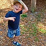 child, boy, smiling, cap, shorts, sneakers, outdoor, forest, leaves, sunlight, happy, playful, nature, person, casual_clothing, daylight, tree_trunks, ground, greenery, young