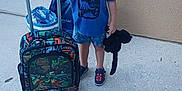 David Leland is registered to the contest to win money with this photo: child, boy, sunglasses, cap, blue_shirt, shorts, sneakers, suitcase, dinosaur, stuffed_animal, outdoor, sidewalk, concrete, wall, travel, smiling, person, summer, luggage, toy