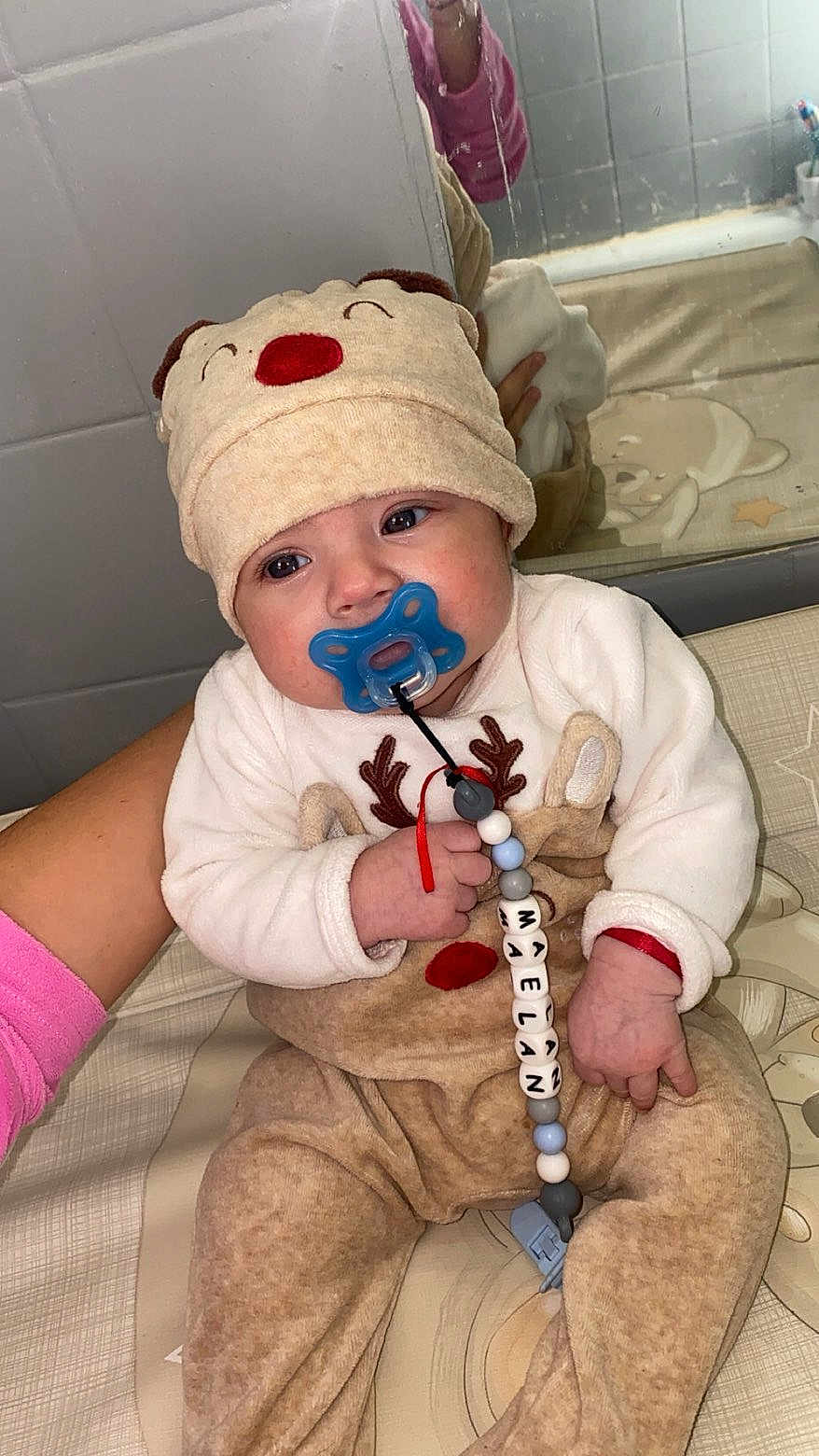 Maëlan participe au concours pour gagner de l'argent avec cette photo : baby, infant, pacifier, hat, reindeer_outfit, clothing, child, cute, indoor, mirror, reflection, hand, holding, beads, toy, person, face, eyes, cozy, seated