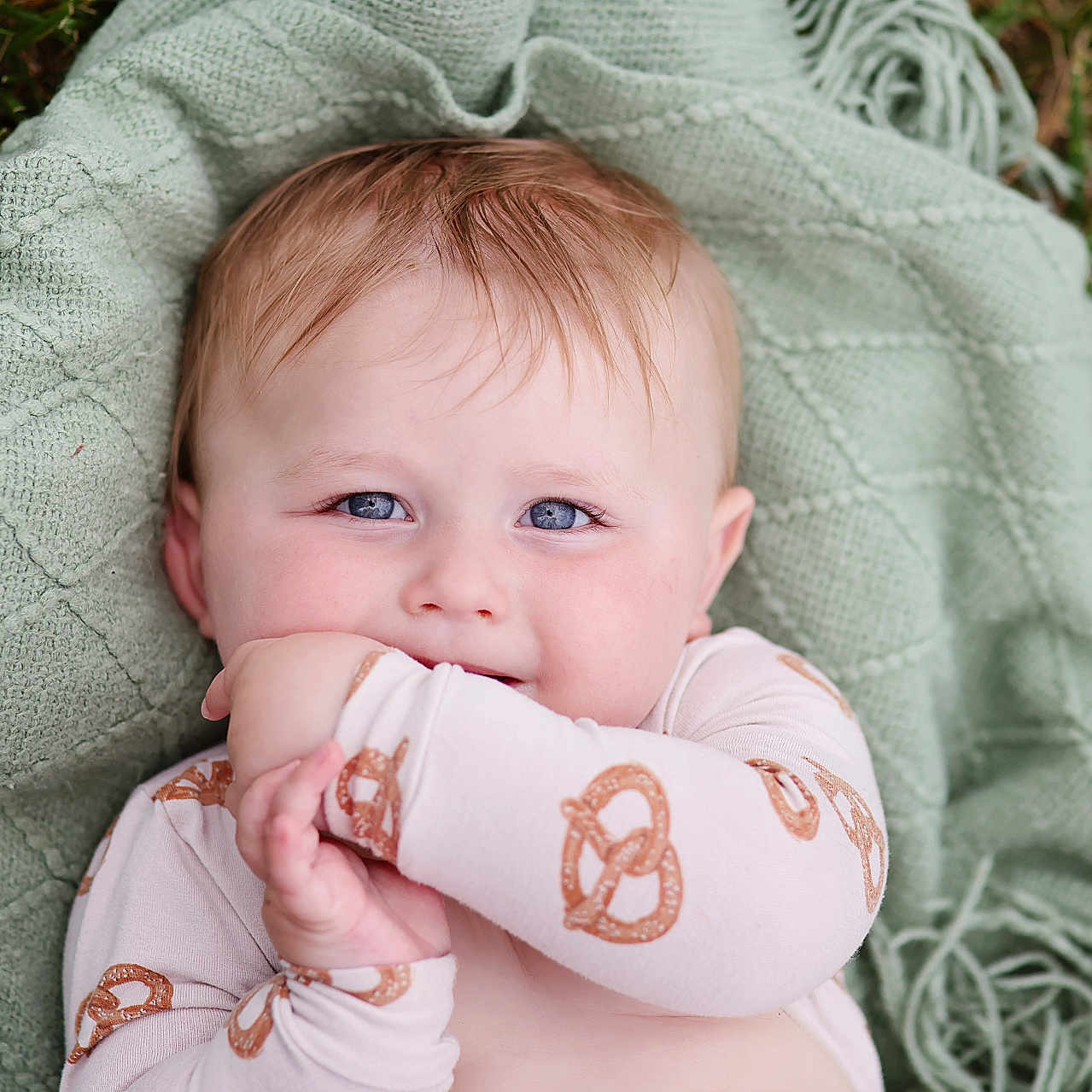 Oaklen is registered to the contest to win money with this photo: baby, child, blue_eyes, blanket, green_blanket, pretzel_pattern, onesie, cute, outdoor, grass, infant, portrait, smiling, happy, soft_light, texture, playful, lying_down, close_up, young_child
