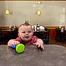 baby, child, toy, table, indoor, restaurant, spiky_hair, happy, smiling, furniture, chairs, lighting, casual, dining, red_shirt, playful, person, face, cute, infant