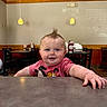 Oaklen is registered to the contest to win money with this photo: baby, child, mohawk, smile, red_shirt, mickey_mouse, table, hand, diner, chair, indoor, lamp, ceiling, face, person, cute, happy, expression, curious, restaurant