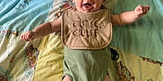 Wilson joined the competition — help win amazing prizes! baby, infant, smiling, bib, green_onesie, blanket, patchwork, cute, happy, arms_outstretched, lying_down, indoor, child, face, skin, head, legs, feet, playful, expression