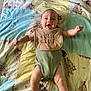 baby, infant, smiling, bib, green_onesie, blanket, patchwork, cute, happy, arms_outstretched, lying_down, indoor, child, face, skin, head, legs, feet, playful, expression