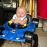 baby, child, toy_car, blue, batman_logo, indoor, floor, stool, red_bin, car_wheels, car_seat, car_toy, car_steering_wheel, car_controls, car_toys, car_body, car_toy_vehicle, person
