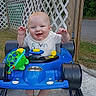 baby, smiling, toy_car, blue, outdoor, fence, wooden, grass, greenery, happy, child, clothing, socks, playing, cute, person, walker, toys, face, baby_girl_or_boy