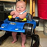 baby, walker, blue, batman, toy, infant, standing, arms_folded, indoor, carpet, stool, storage_bin, plastic, footwear, person, child, face, head, floor, furniture