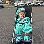child, baby, stroller, dinosaur_costume, hooded_costume, turquoise_costume, smile, happy, sitting, parking_lot, cars, asphalt, wheels, outdoor, fall_trees, parking, cute, infant, hood, portrait
