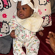 Miracle Bell joined the competition — help win amazing prizes! baby, infant, headband, bib, floral_pajamas, hello_kitty, pillow, hand, maroon_bedspread, cute, indoors, child, portrait, sitting, person, cloth, pattern, pink, white, soft