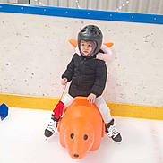 Kayline a rejoint le concours — aidez-le/la à gagner de superbes lots ! black_jacket, child, childrens_toy, fun, helmet, ice, ice_rink, ice_skate, indoor, orange_skating_aid, person, plastic_toy, protective_gear, recreational_activity, red_glove, skating, sports_equipment, white_pants, winter_clothing, young_child