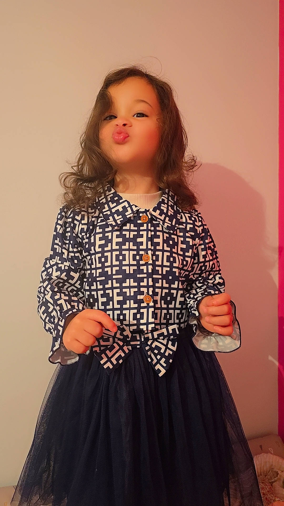 Kayline a rejoint le concours — aidez-le/la à gagner de superbes lots ! bow, buttoned_shirt, child, curly_hair, cute, dress, expression, face, fashion, girl, hands, indoor, long_sleeves, patterned_clothing, portrait, pouting, standing, tulle_skirt, wall, young