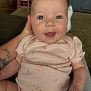 Ella joined the competition — help win amazing prizes! baby, infant, smiling, onesie, peach_pattern, blue_eyes, hand, tattoo, indoor, chair, person, cute, happy, child, skin, face, sitting, apparel, young, holding