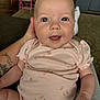 baby, infant, smiling, onesie, peach_pattern, blue_eyes, hand, tattoo, indoor, chair, person, cute, happy, child, skin, face, sitting, apparel, young, holding