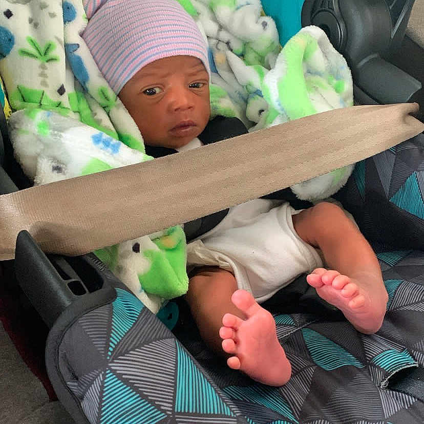 Hassan Taylor is registered to the contest to win money with this photo: baby, infant, child, car_seat, seatbelt, blanket, striped_hat, hat, face, feet, toes, portrait, sitting, indoors, vehicle, newborn, clothing, fluffy_blanket, text_overlay, emoji