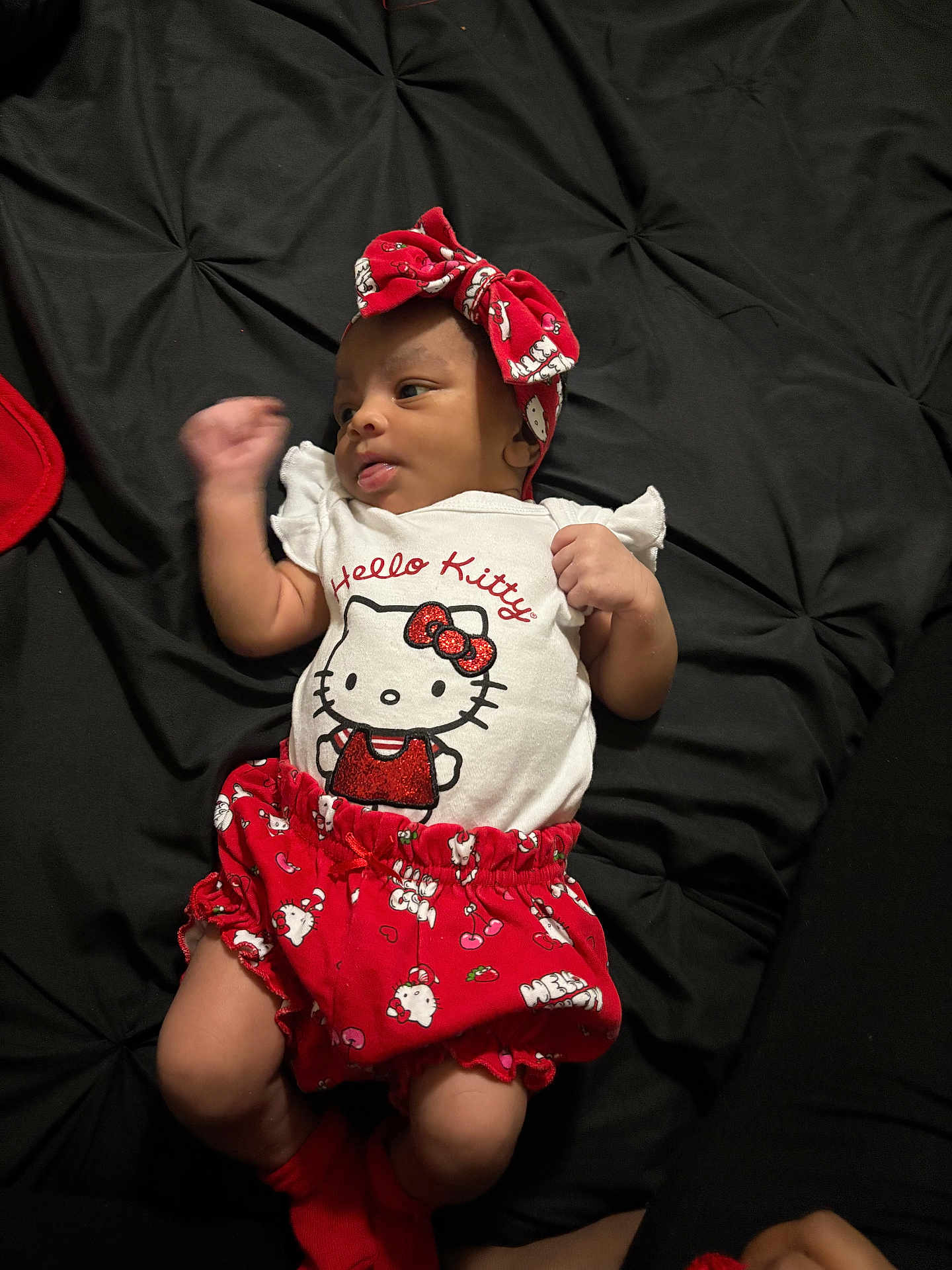 Za'Riyah joined the competition — help win amazing prizes! baby, infant, hello_kitty, red_clothing, headband, lying_down, black_blanket, cute, child, small_fist, looking_sideways, soft_lighting, indoors, adorable, portrait, clothing, sock, infant_girl, comfortable, resting