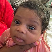 Ashai joined the competition — help win amazing prizes! baby, infant, face, hand, curly_hair, pink_clothing, wide_eyes, expression, cushion, blanket, indoor, person, child, portrait, skin, nail_polish, holding, closeup, cute, young
