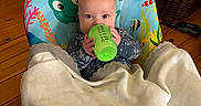 Theodore is registered to the contest to win money with this photo: baby, bottle, blanket, baby_chair, colorful, indoor, wooden_floor, stuffed_animals, basket, clothing, child, person, face, blue_eyes, toy, floor, home, cozy, infant, seating