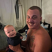 Theodore is registered to the contest to win money with this photo: baby, man, smile, tattoo, shirtless, indoor, curtains, bed, pillow, joy, happiness, person, holding, parent, child, home, cozy, casual, portrait, family