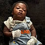 baby, infant, denim_overalls, mittens, black_blanket, cartoon_characters, cute, portrait, child, clothing, soft_texture, indoor, laying_down, serious_expression, person, young_child, casual_wear, closeup, newborn, small_hands