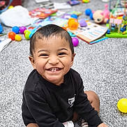 Anantajith joined the competition — help win amazing prizes! toddler, child, smiling, happy, indoor, carpet, toy, colorful, book, sitting, striped_socks, black_sweater, person, playful, cute, young_child, face, hands, feet, room