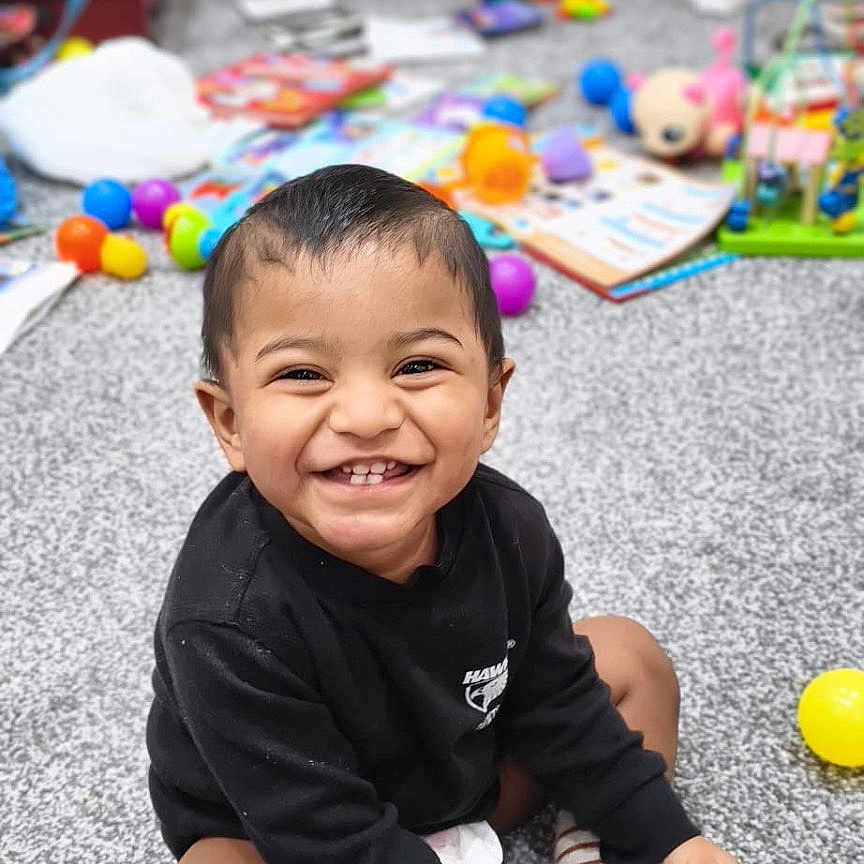 Anantajith joined the competition — help win amazing prizes! black_sweater, book, carpet, child, colorful, cute, face, feet, hands, happy, indoor, person, playful, room, sitting, smiling, striped_socks, toddler, toy, young_child