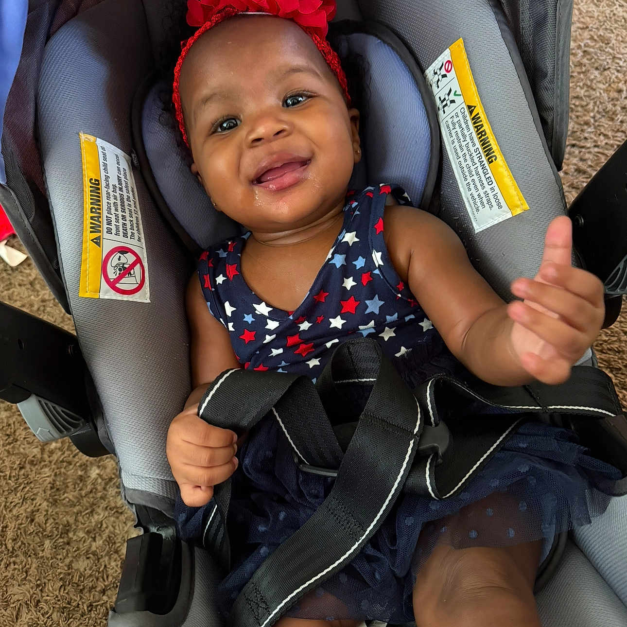 Dajiyah is registered to the contest to win money with this photo: baby, car_seat, carrying_device, child, clothing, cute, dress, face, happy, headband, indoors, infant, person, red_flower, safety_straps, seatbelt, skin, smile, stars, toddler