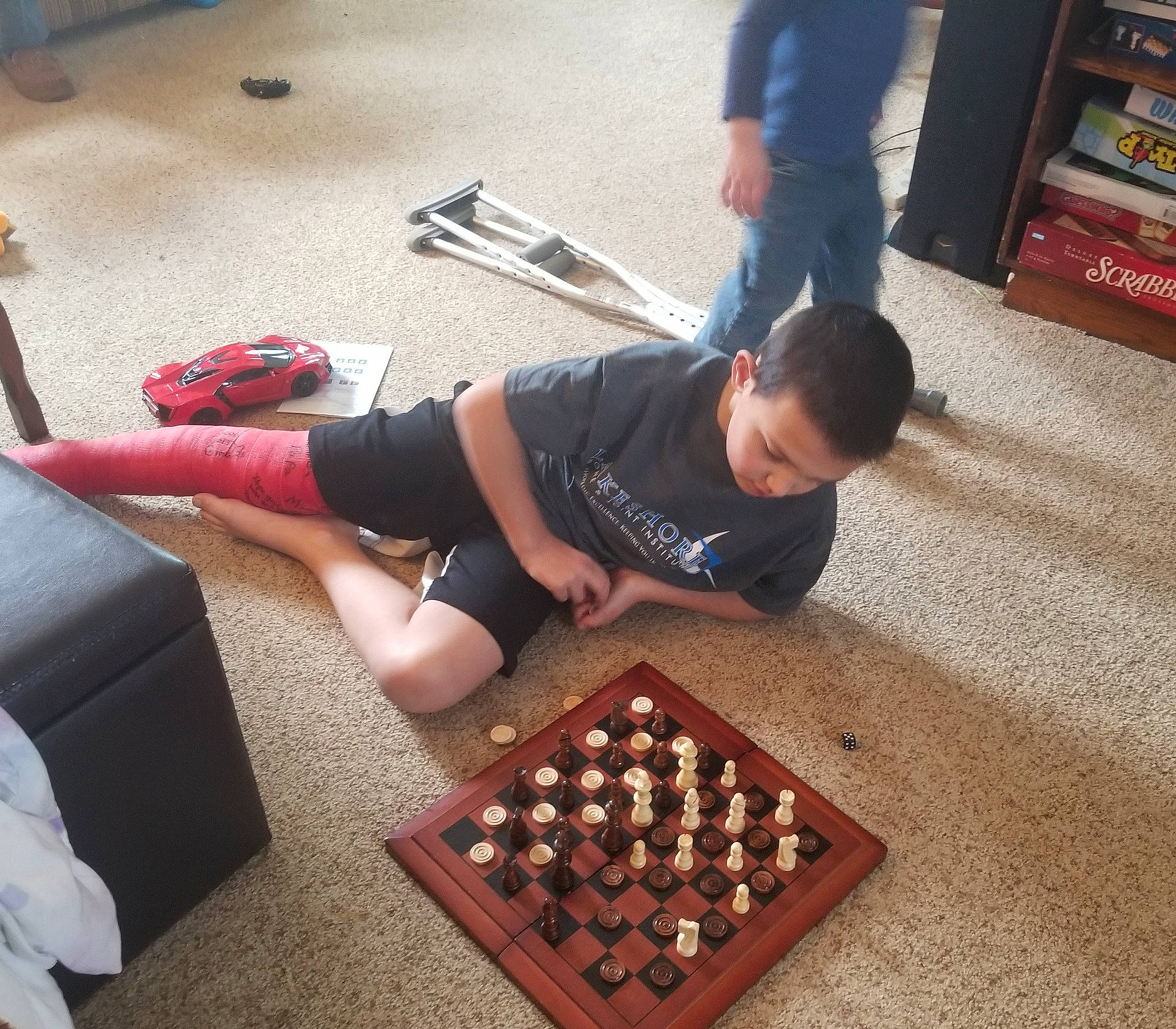 Abel is registered to the contest to win money with this photo: balance, bookcase, chessboard, competition_event, flooring, games, hardwood, human_leg, indoor_games_and_sports, knee, leisure, person, recreation, shelf, shelving, shorts, sunglasses, t_shirt, table, thigh