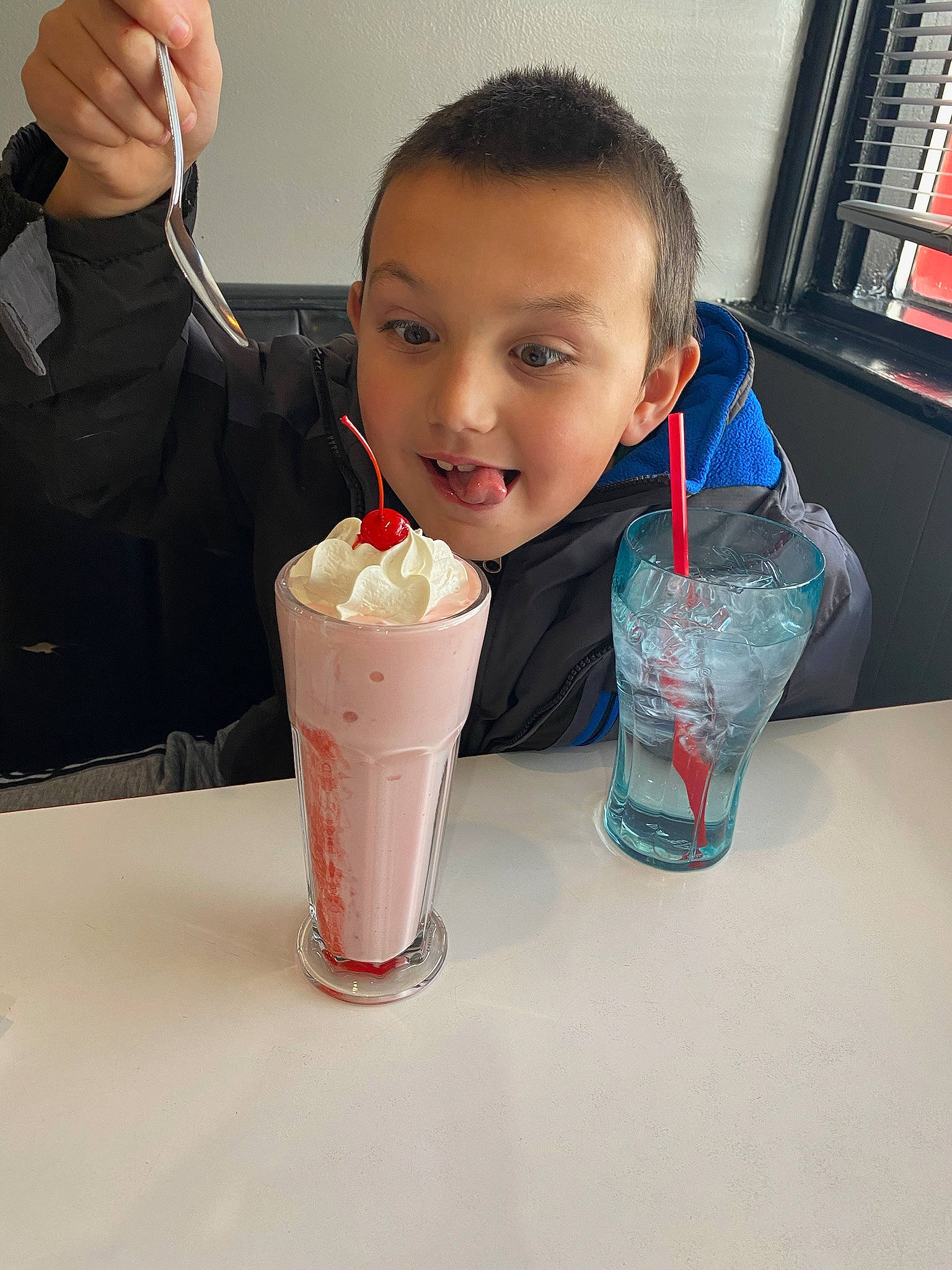 Abel is registered to the contest to win money with this photo: bookcase, cream, dairy, drink, drinking, drinking_straw, drinkware, food, gelato, gesture, hand, ice_cream, ingredient, joy, milkshake, person, shelf, smile, soft_drink, sweetness