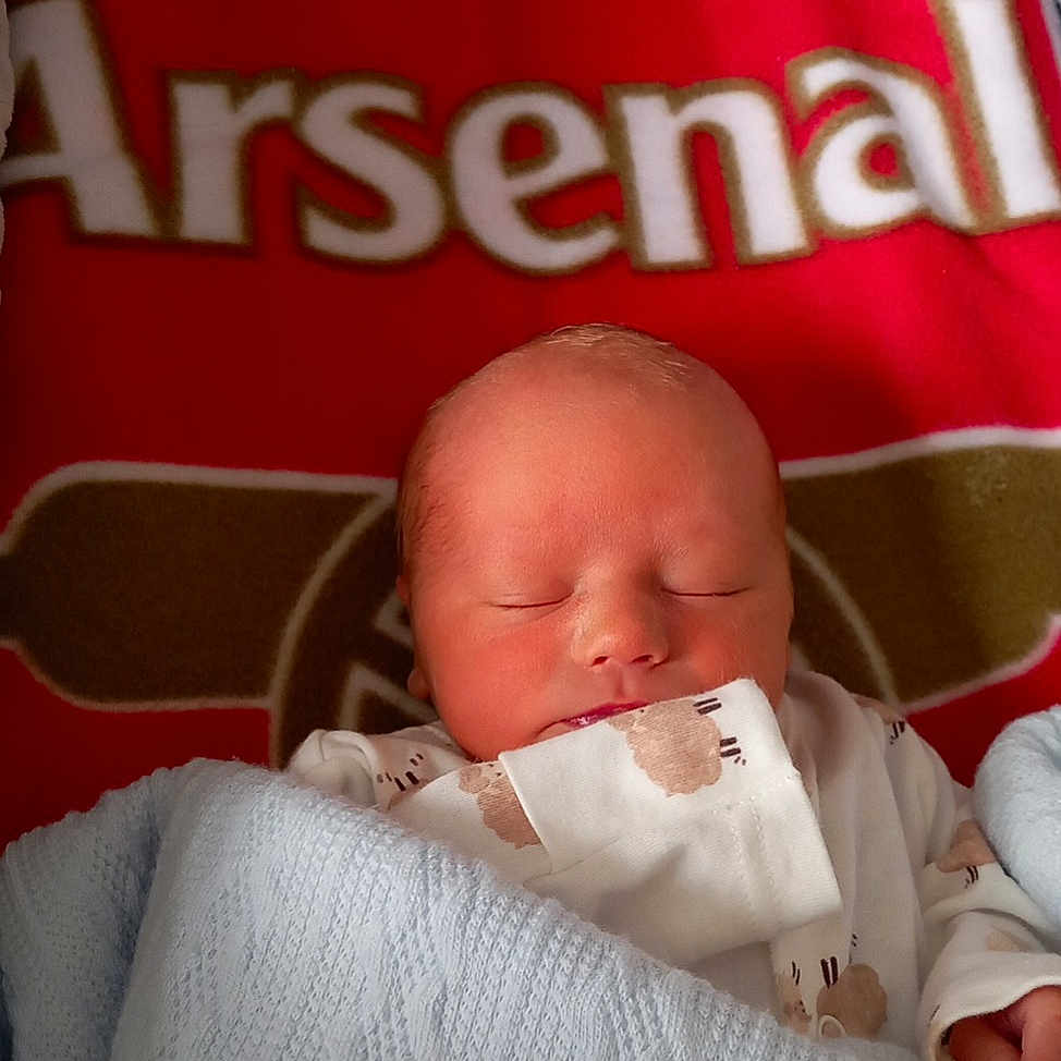 Oscar is registered to the contest to win money with this photo: arsenal, baby, bed, blanket, blue_blanket, clothing, cozy, cute, face, head, indoors, infant, newborn, peaceful, portrait, resting, sleeping, soft_texture, sports_logo, wrapped