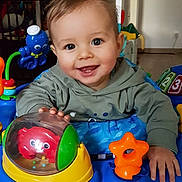 Milo a rejoint le concours — aidez-le/la à gagner de superbes lots ! baby, child, smiling, face, indoor, toy, activity_walker, play, colorful, happy, hoodie, hand, floor, plastic_toy, octopus_toy, star_toy, red_toy, blue_toy, person, infant