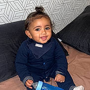 Ya-Sine participe au concours pour gagner de l'argent avec cette photo : baby, bed, blanket, blue_bottle, bottle, child, clothing, cute, face, geometric_pattern, hair_topknot, happy, indoor, infant, onesie, pillow, sitting, smile, socks, wallpaper
