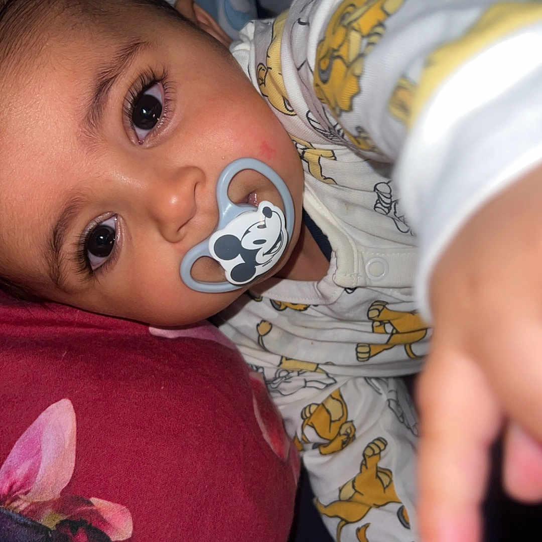 Ya-Sine participe au concours pour gagner de l'argent avec cette photo : baby, bed, blanket, child, close_up, cushion, cute, expression, face, hand, indoors, infant, lying_down, mickey_mouse, pacifier, pajamas, portrait, reaching, sleepwear, soft_lighting