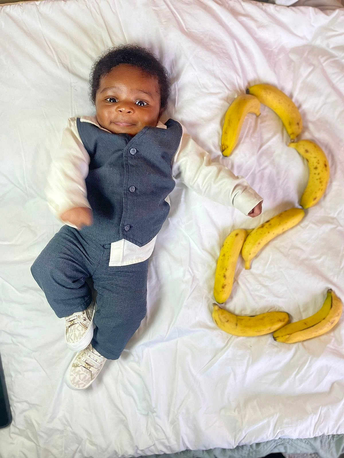 Naël a rejoint le concours — aidez-le/la à gagner de superbes lots ! baby, infant, child, suit, clothing, white_sheet, bananas, fruit, number_three, lying_down, smiling, cute, footwear, shoes, indoor, portrait, face, happy, young, playful