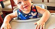 Niko joined the competition — help win amazing prizes! toddler, child, high_chair, smiling, blue_eyes, tank_top, restaurant, table, chair, wood_floor, window, daylight, cute, happy, indoor, person, furniture, skin, face, hands