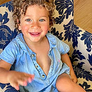 Leon participe au concours pour gagner de l'argent avec cette photo : child, toddler, curly_hair, blue_eyes, smiling, armchair, blue_shirt, happy, indoor, cute, portrait, person, furniture, hand, skin, buttoned_shirt, seat, playful, baby, young_child