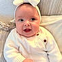 Dua is registered to the contest to win money with this photo: baby, child, smiling, headband, bow, white_sweater, couch, pillow, closeup, indoor, happy, infant, cute, portrait, soft_lighting, cozy, furniture, person, skin, hand